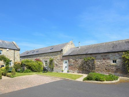 Stone cottages with paved driveway and garden with shrubs and lawn at Lavender Cottage Village Farm in Seahouses