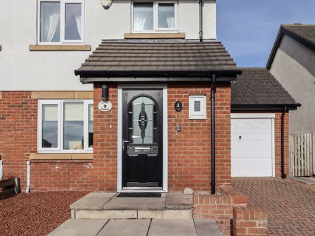 Front door entrance of a house with black door and brick walls at Sandy Shores in Seahouses