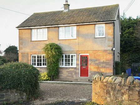 A two storey house with white framed windows a red front door and stone wall in front at Barmoor in Embleton