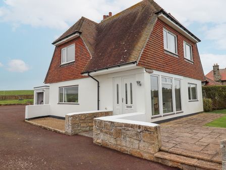 A two story house with tiled roof white walls stone fence and paved driveway at Whitestacks in Bamburgh