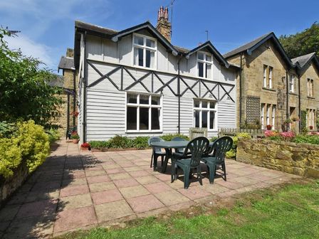 A patio area with a plastic table and chairs outside a house with white wooden siding and stone walls at Garden House in Alnmouth