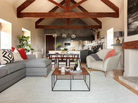 A living room with a gray sectional sofa and armchair a wooden coffee table with decor and an open kitchen with a dining table and chairs at Lantern View in Eglingham