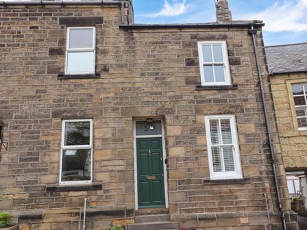 A stone house exterior with a green front door and white framed windows at Strandline in Alnmouth