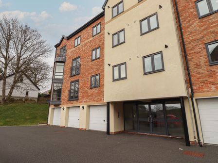 An exterior view of a multi-story residential building with brick and beige walls garages and glass entrance doors at Assisi Apartment in Alnmouth