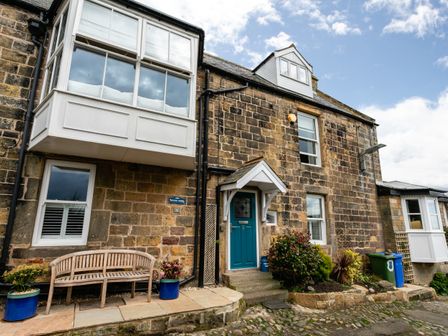 Stone exterior of a house with a blue door a wooden bench and potted plants at Begonia House in Alnmouth
