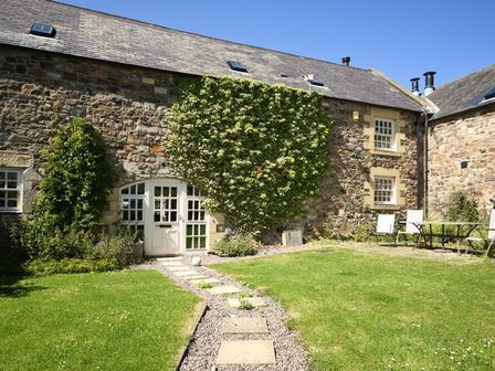 An outdoor garden with grass stone pathway table and chairs and stone building at Budle Granary Bamburgh