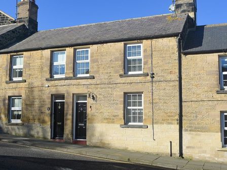 Stone terraced houses with black doors and white window frames on a street at Crier Cottage in Alnwick