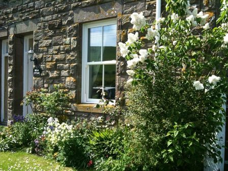A stone wall cottage exterior with white window and garden plants with white flowers at Briar Cottage in Town Yetholm and Kirk Yetholm
