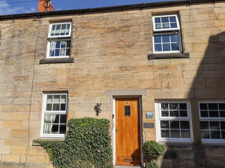 Front of a stone cottage with a wooden door and four windows at Dray Cottage in Warkworth
