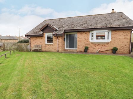 A front yard with grass lawn and a bench outside a brick house at Dunes Cottage in Beadnell
