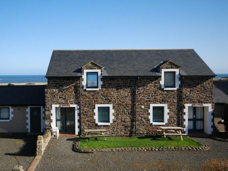 A stone house with two picnic benches on grass and a view of the sea at Fidra in Embleton