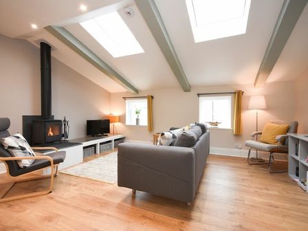 A living room with a gray sofa a wood stove and wooden floors at Herringbone Cottage in Seahouses