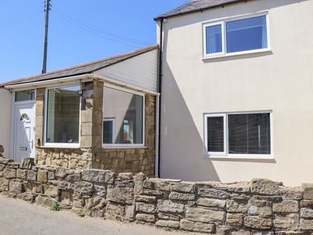 The exterior of a house with stone and white walls windows and a low stone wall by the roadside at Island View in Amble