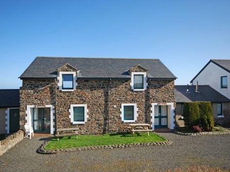 A stone house with two entrances and green picnic tables on grass at Longstone in Embleton