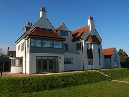 A large white house with red roof tiles and green window frames on a grassy lawn at Sandpiper Bamburgh