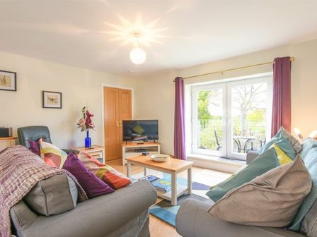 A living room with two sofas, a coffee table, a television, purple curtains, and a glass door at Schooner Court No1 in Alnmouth