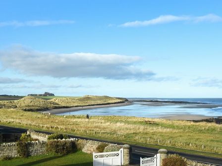 A coastal landscape with sandy dunes grass and a road in the foreground and sea in the background at Ty y Mor in Seahouses