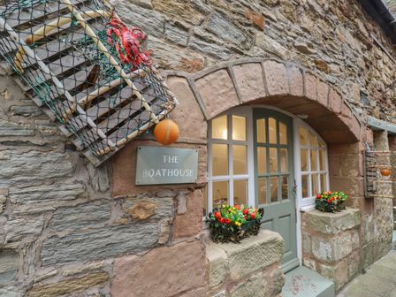 Stone building entrance with arched doorway and lobster pots hanging beside a sign reading The Boathouse at The Boathouse Seahouses