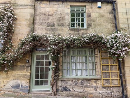 A stone house exterior with a green door and windows covered with flowering vines at The Book House in Warkworth