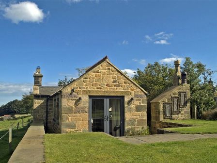 A stone cottage with a glass door in a grassy area at The Huffy House in Alnmouth