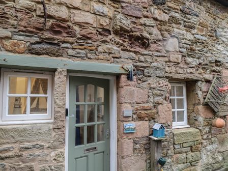 A stone exterior wall with a green door and two white framed windows with nautical decorations at The Little Boathouse in Seahouses