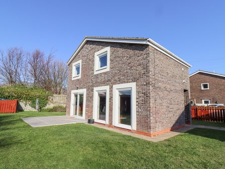 A brick two story house with windows and a sliding door and a lawn at Tree Corner in Beadnell