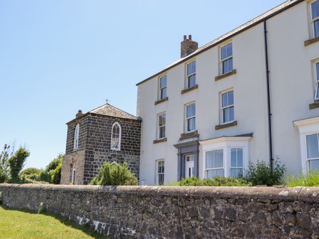 A large stone and white building with multiple windows and a garden wall at The Lookout Embleton