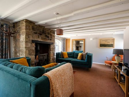 A living room with two teal sofas a stone fireplace and an orange chair at The Arches in Bamburgh