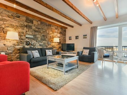 A living room with sofas a stone wall wooden beams and a large window at Farne Lookout in Seahouses