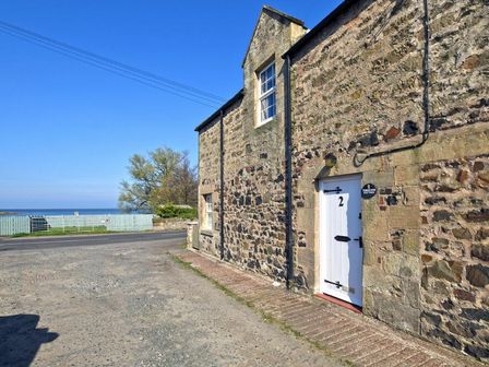 The exterior of a stone house with a white door numbered 2 near a road and a view of the sea at Turnstone Cottage Nr Bamburgh