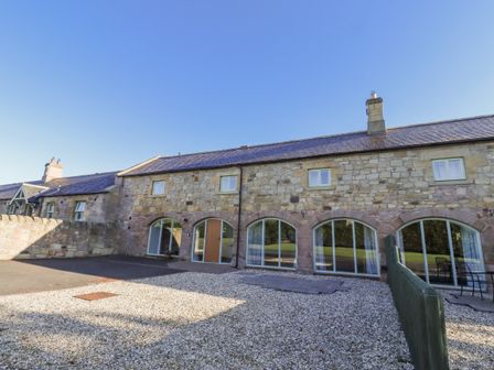 An outdoor area with a stone wall and large windows at Goldfinch in Lucker