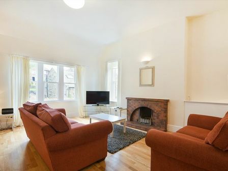 A living room with two brown sofas a brick fireplace a television on a stand and windows with white curtains at Decked Out in Alnmouth