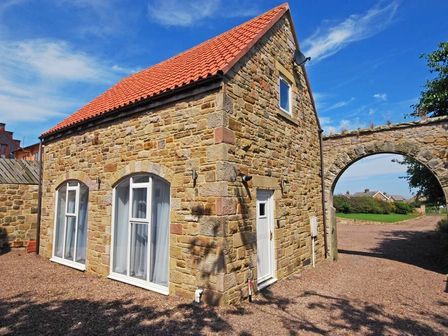 A stone house with arched windows and a red tiled roof next to a stone archway at Quarry Mews in Bamburgh