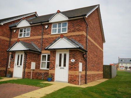 A semi detached brick house with a white front door and pathway at House Martins Beadnell