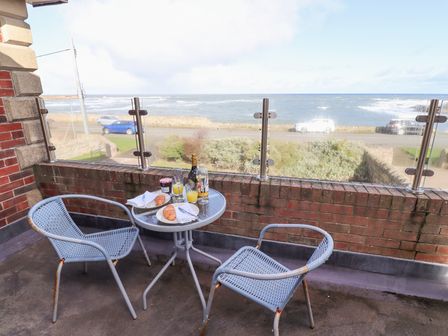 A balcony with two chairs and a small round table set with croissants drinks and jam overlooking the sea at Rathowen in Beadnell