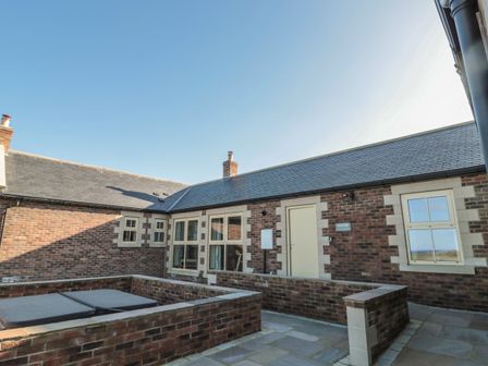An outdoor patio area with brick walls and multiple windows at Nook Cottage in Embleton