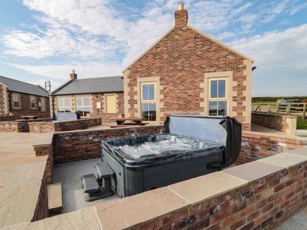 An outdoor hot tub with steps surrounded by brick walls and a brick house in the background at Smithy Cottage in Embleton