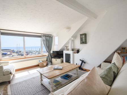 A living room with a large window overlooking boats and water with sofas a wooden coffee table and a small television at The Penthouse @ No 5 in Lyme Regis