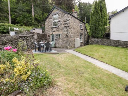 A stone cottage with a small patio dining set and garden path at Bron Celyn Bach in Betws-Y-Coed