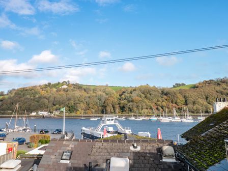 A harbor with boats and cars parked near a body of water with hills and trees in the background at Aloft in Dartmouth