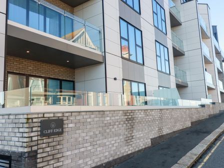 A modern apartment building with glass balconies and a brick wall with a cliff edge sign in Newquay