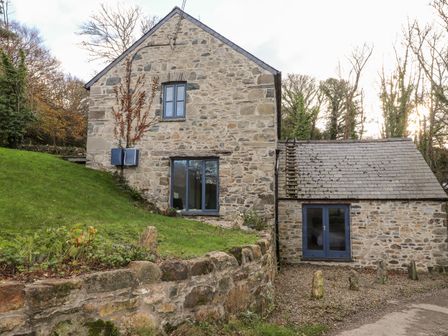 A stone house with slate roof and blue windows surrounded by grass and trees at Castle Mill in Newport Pembrokeshire