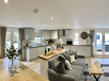 An open plan kitchen and living room with gray cabinets a wooden countertop a gray sofa and wooden tables at Abode Raymond's Hill