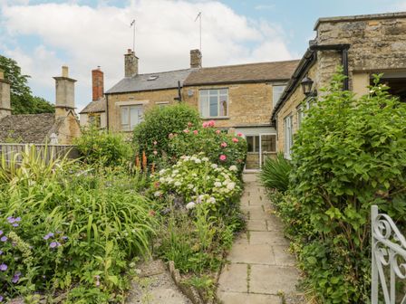 A garden with flowers and bushes along a stone pathway leading to a stone house at 2 Church Street in Chipping Norton