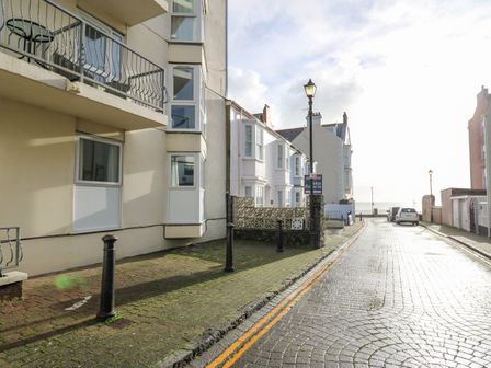 A street with parked cars buildings on either side and a view of the sea at 1 St Marys Court in Tenby
