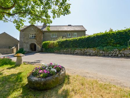 A farmhouse with a driveway and stone flower planters with flowers and a hedge at Twelve Oaks Farmhouse in Teigngrace near Newton Abbot