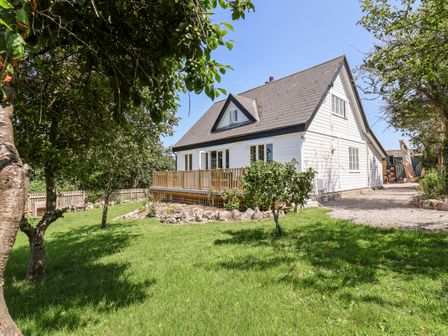 A white house with a gable roof and wooden deck in a yard with grass and trees at Melbecks in Abergele
