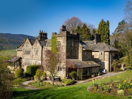 A stone house with chimneys surrounded by garden and trees at Kail House in Grassington