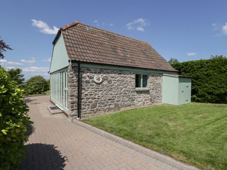 A stone building with green doors and window beside a paved pathway and lawn at Swallow Barns in Chipping Sodbury