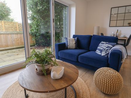 A living room with a blue sofa, round wooden coffee table with a plant, and woven pouf at The Bungalow in Lyme Regis